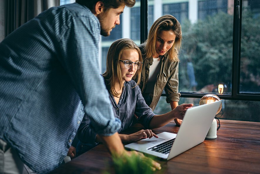 eine junge Frau vor dem Laptop mit einem jungen Mann rechts daneben und eine Frau links von ihr
